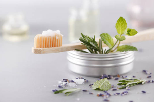 Natural toothpaste in a metal tin with bamboo toothbrush, fresh mint, rosemary, and lavender — zero-waste oral care.